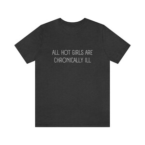 May include: A dark heather grey t-shirt with the text "ALL HOT GIRLS ARE CHRONICALLY ILL" printed in white.