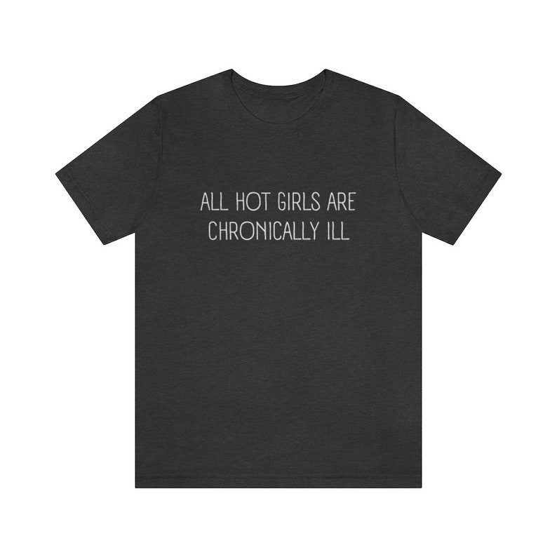 May include: A dark heather grey t-shirt with the text "ALL HOT GIRLS ARE CHRONICALLY ILL" printed in white.