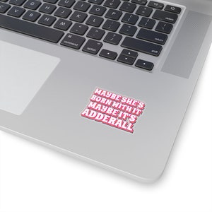 May include: A sticker with the text "Maybe she's born with it, maybe it's Adderall" in pink and white letters on a silver laptop.