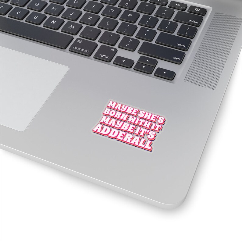 May include: A sticker with the text "Maybe she's born with it, maybe it's Adderall" in pink and white letters on a silver laptop.