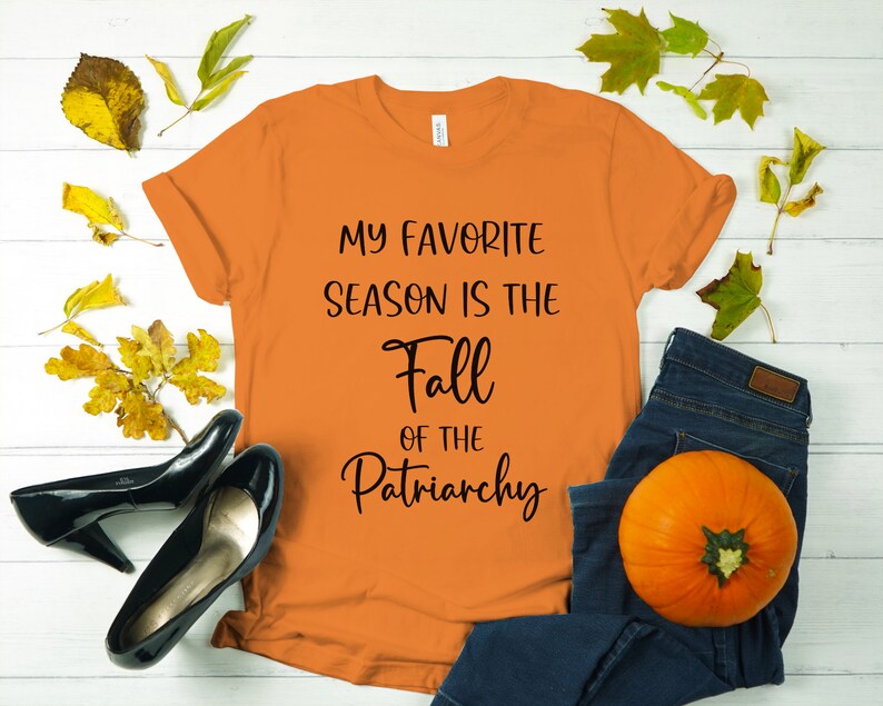 Op de afbeelding: Oranje T-shirt met de tekst "My favorite season is the Fall of the Patriarchy" in zwart gedrukt.