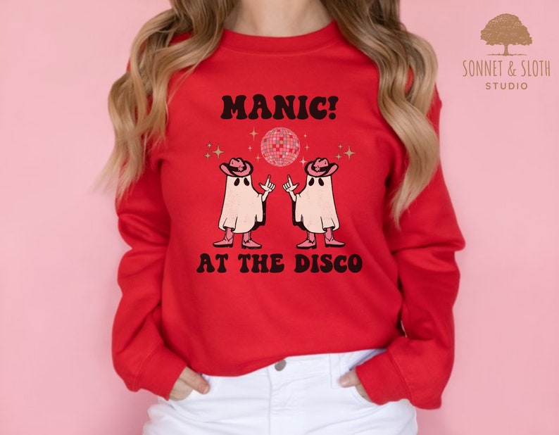 May include: Red sweatshirt with a white graphic of two ghosts wearing cowboy hats and dancing in front of a disco ball. The text "MANIC! AT THE DISCO" is printed in black below the ghosts.