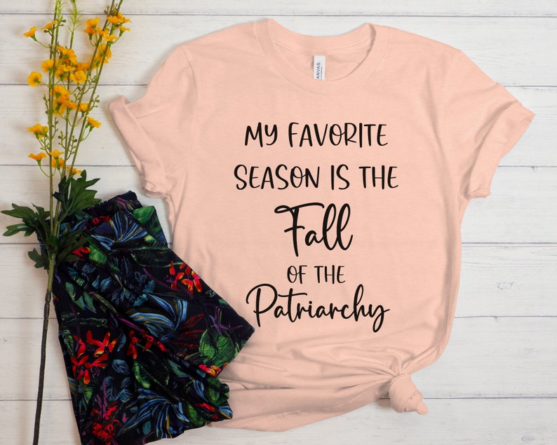 Op de afbeelding: Een perzikkleurig T-shirt met de tekst "My favorite season is the Fall of the Patriarchy" in zwart gedrukt.
