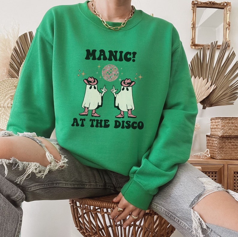 May include: Green sweatshirt with a graphic of two ghosts wearing cowboy hats and dancing. The text "MANIC! AT THE DISCO" is printed on the sweatshirt.