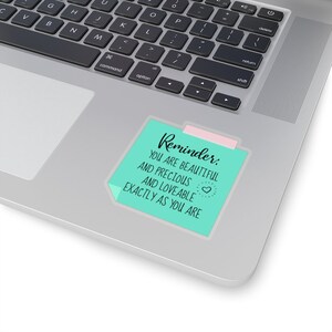May include: A teal blue sticky note with a pink tab on a laptop. The note says "Reminder: You are beautiful and precious and loveable exactly as you are."