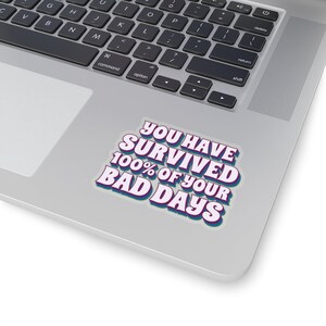 May include: A white sticker with blue and purple text that reads "You Have Survived 100% Of Your Bad Days".