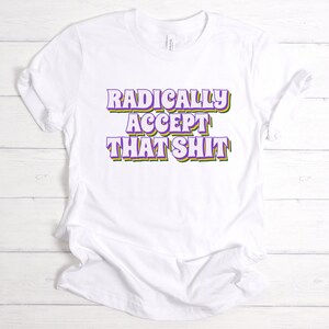 May include: White t-shirt with the text "RADICALLY ACCEPT THAT SHIT" in purple, green, and yellow letters.