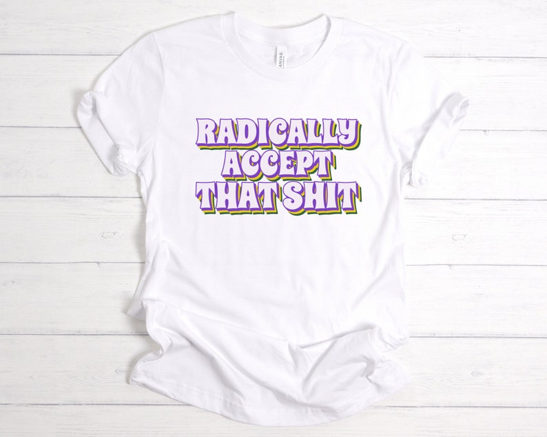 May include: White t-shirt with the text "RADICALLY ACCEPT THAT SHIT" in purple, green, and yellow letters.