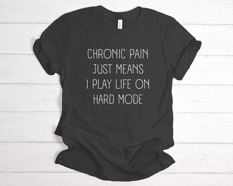 May include: Black t-shirt with white text that reads "Chronic pain just means I play life on hard mode."