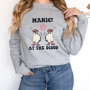 May include: A gray sweatshirt with the text "MANIC! AT THE DISCO" and a graphic of two ghosts wearing cowboy hats and holding disco balls.