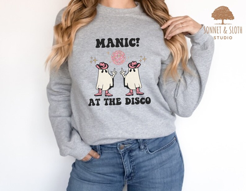 May include: A gray sweatshirt with the text "MANIC! AT THE DISCO" and a graphic of two ghosts wearing cowboy hats and holding disco balls.
