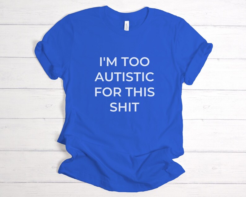 Puede incluir: Camiseta azul real con el texto blanco "I'M TOO AUTISTIC FOR THIS SHIT". La camiseta es de cuello redondo y parece estar hecha de un material suave. La camiseta est&aacute; doblada sobre una superficie de madera clara.