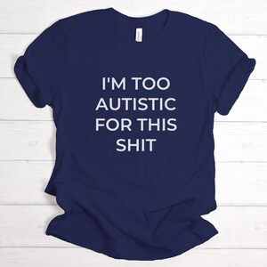 Puede incluir: Camiseta azul marino con el texto blanco "I'M TOO AUTISTIC FOR THIS SHIT". La camiseta est&aacute; hecha de un material suave y tiene las mangas enrolladas. Es una prenda informal.