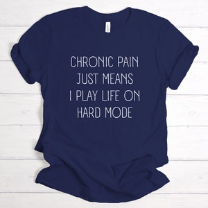 May include: Navy blue t-shirt with white text that reads "Chronic pain just means I play life on hard mode".