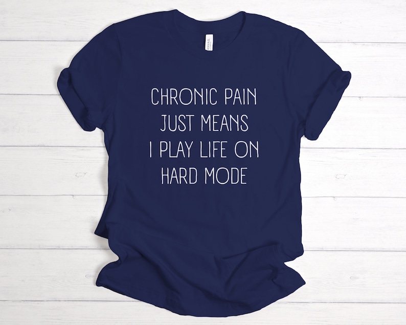 May include: Navy blue t-shirt with white text that reads "Chronic pain just means I play life on hard mode".