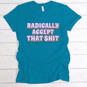 May include: Teal blue t-shirt with the text "RADICALLY ACCEPT THAT SHIT" in a retro font with purple and yellow outlines.