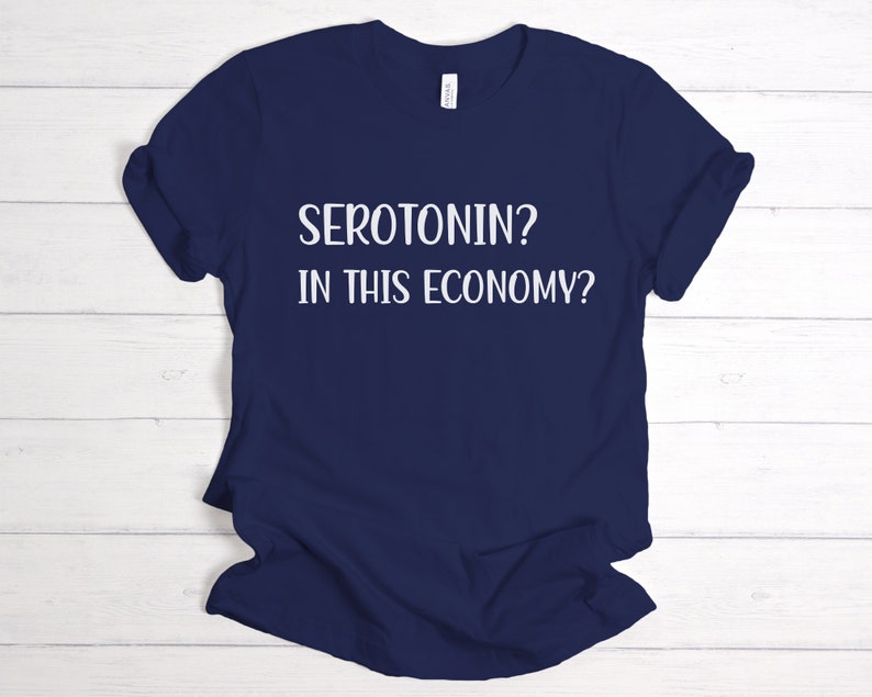 Pu&ograve; includere: Maglietta blu navy con testo bianco che dice "SEROTONIN? IN THIS ECONOMY?"