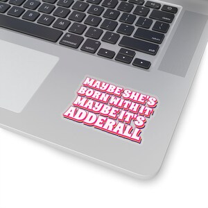 May include: A sticker with the text "Maybe she's born with it maybe it's Adderall" in a retro font style. The text is pink with a yellow outline and a blue shadow.