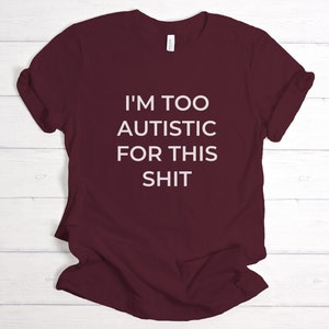 Puede incluir: Camiseta granate con la frase blanca "I'M TOO AUTISTIC FOR THIS SHIT". La camiseta de cuello redondo est&aacute; hecha de un material suave. El texto est&aacute; centrado en la parte delantera de la camiseta. La camiseta es de color rojo oscuro.