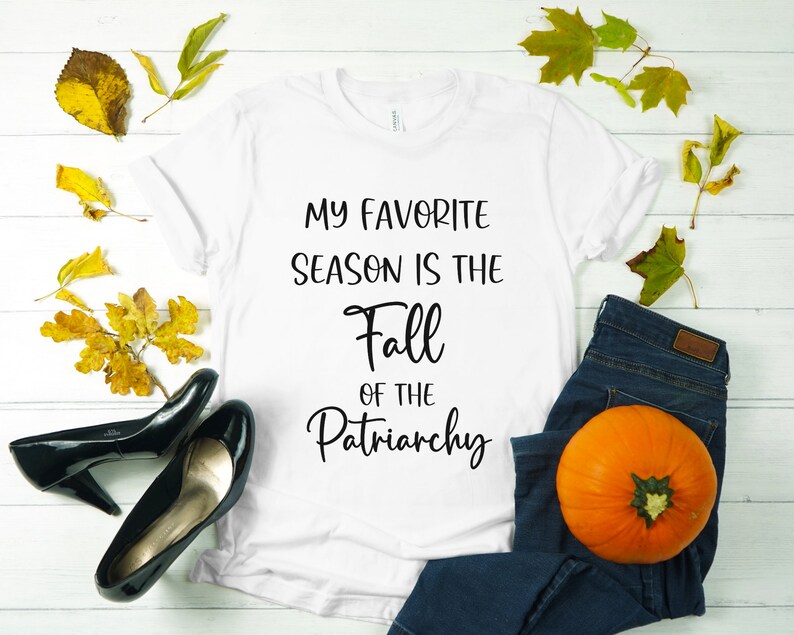 Op de afbeelding: Wit T-shirt met de tekst "My favorite season is the Fall of the Patriarchy" in zwart gedrukt.