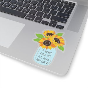 May include: A blue mason jar with a bouquet of yellow sunflowers and green leaves. The jar has the text "If you need a sign, this is it. Please don't give up."