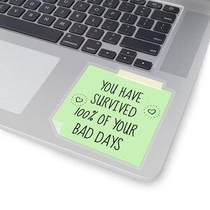 May include: A green sticky note with the text "You have survived 100% of your bad days" on a silver laptop.