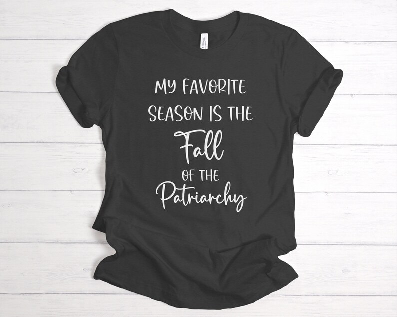 Op de afbeelding: Zwart T-shirt met witte tekst die luidt: "Mijn favoriete seizoen is de val van het patriarchaat."
