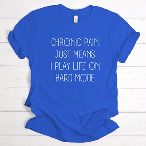 May include: A royal blue t-shirt with white text that reads "Chronic pain just means I play life on hard mode".