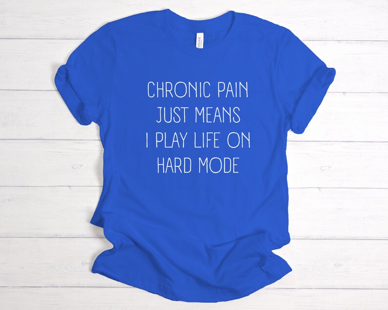 May include: A royal blue t-shirt with white text that reads "Chronic pain just means I play life on hard mode".