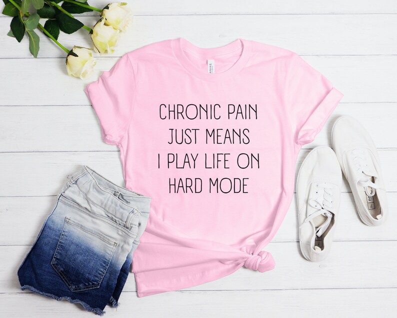 May include: Pink t-shirt with the text "Chronic pain just means I play life on hard mode" printed in black.
