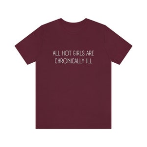 May include: Burgundy t-shirt with the text "ALL HOT GIRLS ARE CHRONICALLY ILL" printed in white.