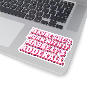 May include: A pink and yellow sticker with the text "Maybe she's born with it maybe it's Adderall" in a retro font style.