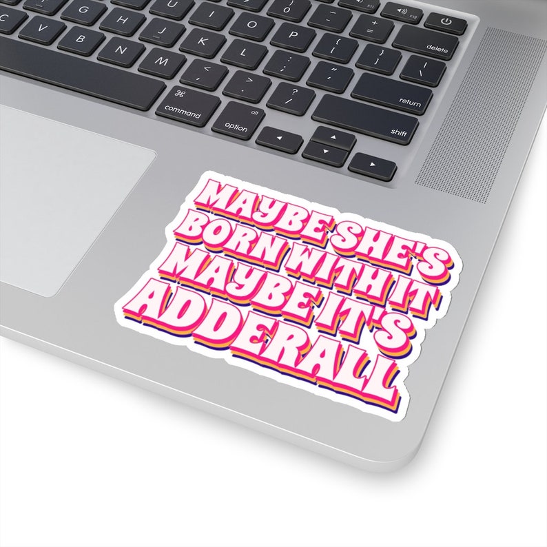 May include: A pink and yellow sticker with the text "Maybe she's born with it maybe it's Adderall" in a retro font style.