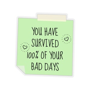 May include: A green sticky note with the text "You have survived 100% of your bad days" with two small hearts drawn on the note.