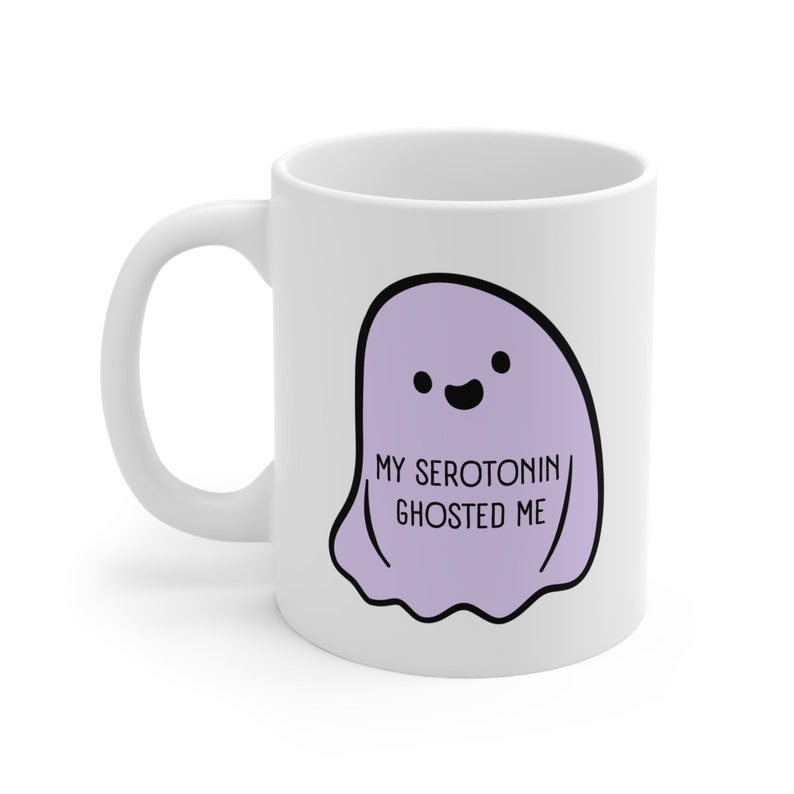 A white ceramic mug with a picture of a purple ghost. Text on the ghost reads, "My serotonin ghosted me."