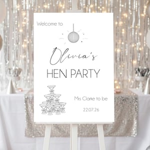 Peut inclure: Un chevalet blanc présente une affiche avec le texte "Welcome to Olivia's HEN PARTY". L'affiche comprend une illustration de boule à facettes et une tour de verres à champagne. Des ballons argentés, blancs et or rose décorent l'arrière-plan.