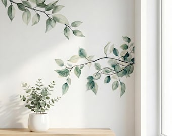 Pode incluir: Decalques de parede de ramos com folhas em estilo aquarela em tons de verde e cinza. Uma pequena planta em vaso com folhas verdes está em uma prateleira de madeira. A parede é branca e uma janela é visível à direita.