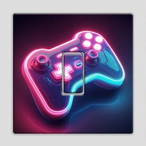 May include: A neon-style light switch cover with a video game controller design. The controller is outlined in pink and blue neon lights, set against a black background. The switch is a white rectangle with a pink cross and circle design.