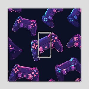 May include: A decorative light switch cover featuring a pattern of stylized purple and blue video game controllers on a dark blue background. The cover has a silver-colored frame around the switch opening.