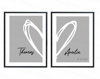 Op de afbeelding: Twee ingelijste kunstdrukken met zwarte lijsten. Elke print heeft een wit hartontwerp op een grijze achtergrond. Eén print zegt "Thomas" en de andere "Amelia" met "est 21.08.20".