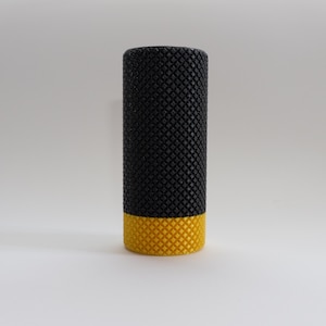 Op de afbeelding: Een zwarte en gele foamroller met een textuur.