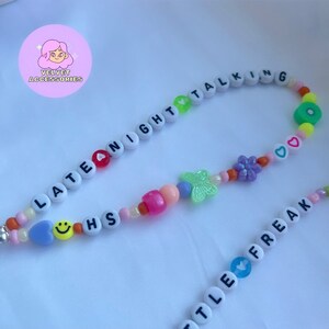 May include: A colorful beaded necklace with the words "Late Night Talking" and "Little Freak" spelled out. The necklace also features a butterfly charm, a flower charm, and a smiley face charm.