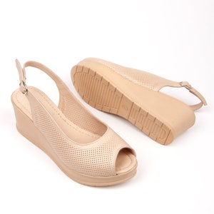May include: A pair of beige peep-toe wedge sandals with a slingback strap and a perforated design.