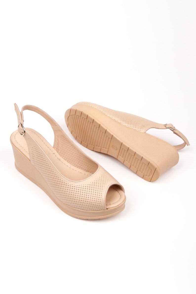 May include: A pair of beige peep-toe wedge sandals with a slingback strap and a perforated design.