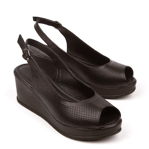 Op de afbeelding: Zwarte leren peeptoe wedgesandalen met een slingback-bandje en een geperforeerd ontwerp.