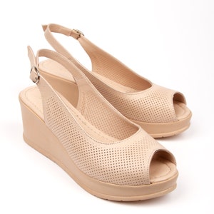 May include: Beige peep-toe wedge sandals with a slingback strap and a perforated design.