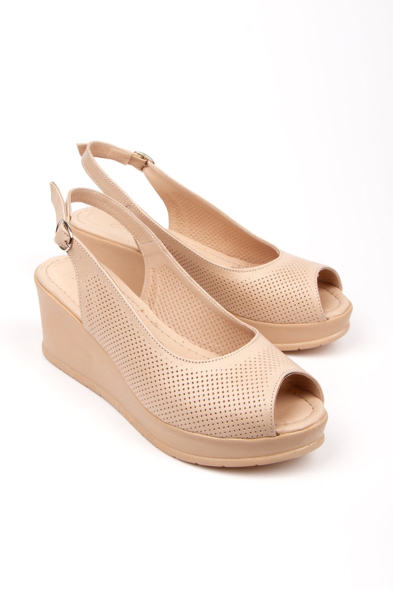May include: Beige peep-toe wedge sandals with a slingback strap and a perforated design.