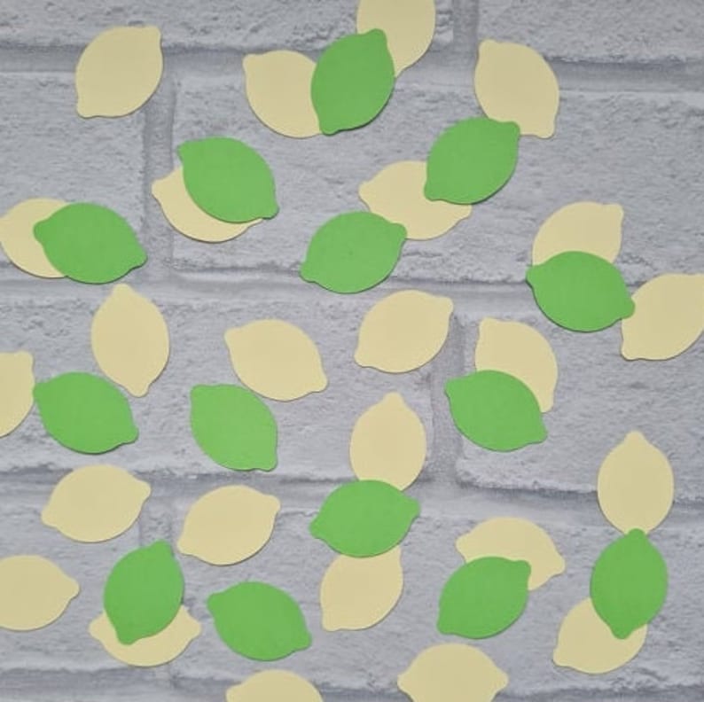 May include: A collection of lime green and yellow paper cutouts shaped like lemons. The cutouts are scattered on a white brick background.