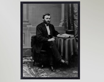 Pode incluir: Fotografia em preto e branco de um retrato de um homem com barba sentado numa cadeira com um livro numa mesa à sua frente.