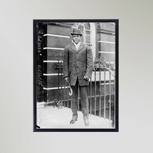 Peut inclure: Une photographie en noir et blanc d'un homme en costume et chapeau, debout devant un bâtiment avec un portail. Le bâtiment porte l'inscription "Clifton Ho" sur le côté.
